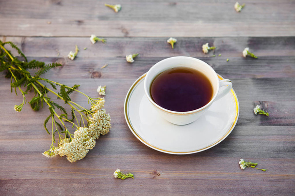 Tasse Tee auf einem Holztisch, mit weißen Blumen - Foto, Bild
