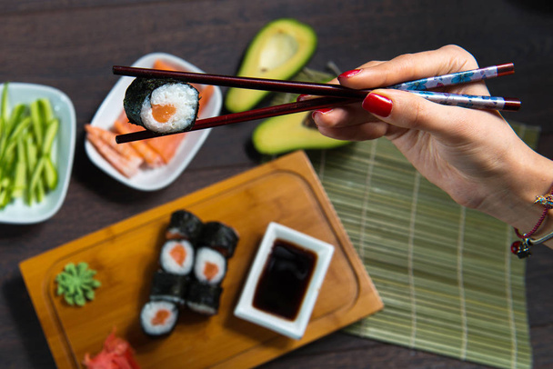La mujer toma los rollos de sushi usando palillos. Fondo negro
 - Foto, imagen