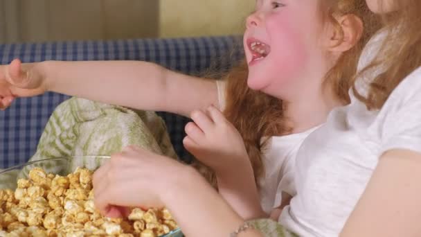 Happy loving family. Mother and her daughter child girl are eating popcorn on the bed in the room. front of the TV - Πλάνα, βίντεο