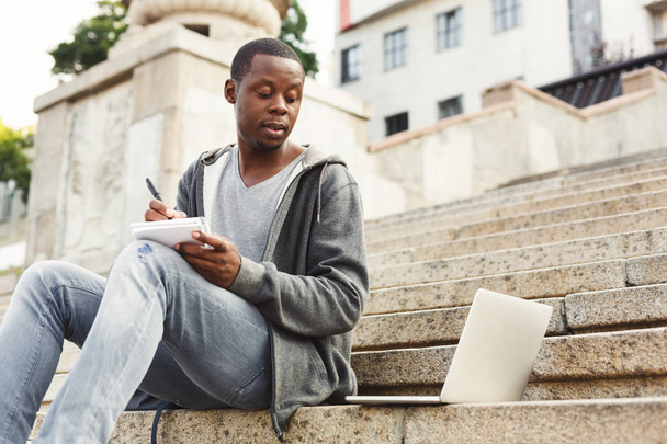 Afrikalı-Amerikalı öğrenci ile laptop ve defter açık havada konsantre - Fotoğraf, Görsel