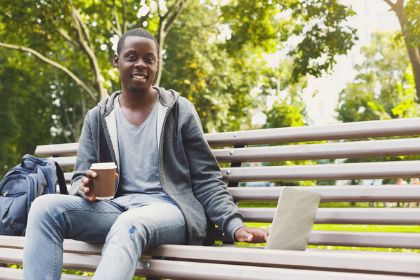 Estudiante afroamericano trabajando en un portátil y tomando café afuera
 - Foto, Imagen