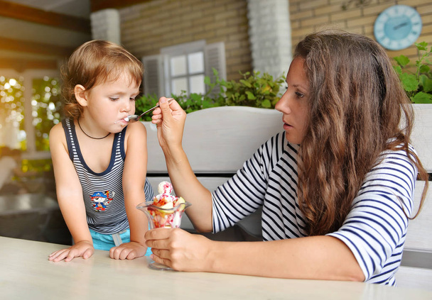 mãe alimenta um jovem filho com sorvete em um café
 - Foto, Imagem