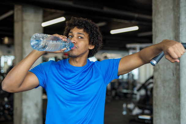 Красивый молодой человек пьет воду в спортзале
 - Фото, изображение