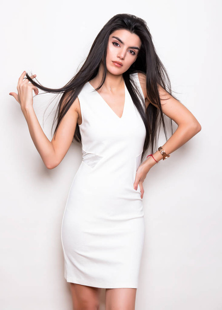 beautiful young woman with long black hair wearing dress and posing on white background - Фото, изображение