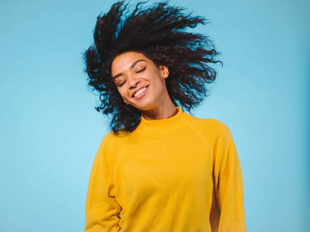 mixed race black woman portrait with big afro curly hair on blue background dancing and with hairstyle flying in air - Zdjęcie, obraz