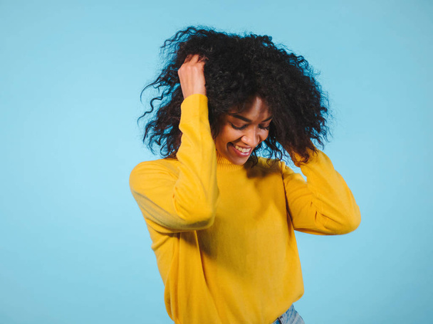 mixed race black woman portrait with big afro curly hair on blue background dancing and with hairstyle flying in air - Photo, Image
