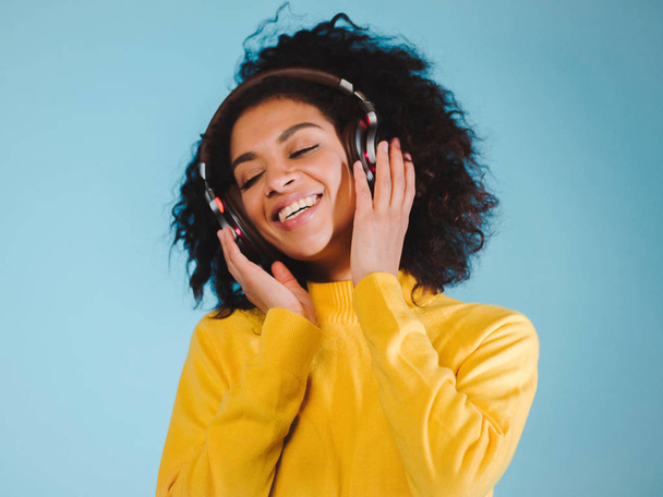 Joy and music. Colorful studio portrait of happy afro young brunette woman with earphones is dancing and singing. - Foto, Imagen