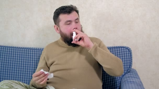 Een man met een verkoudheid zit op de Bank. Hij besprenkelt een speciale neusspray in zijn neus. - Video