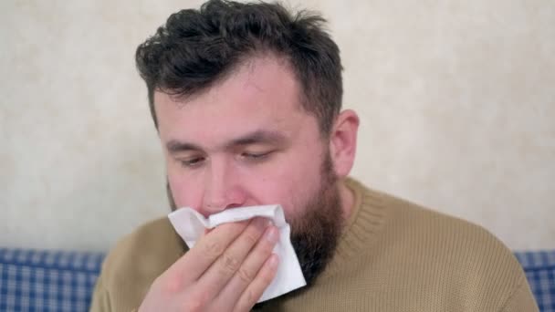 healthcare, flu, hygiene and people concept - sick man blowing nose to paper napkin at home - Кадри, відео