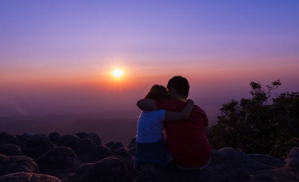 Bruder und Schwester sitzen auf einem Felsen und sehen gemeinsam den Sonnenuntergang bei su - Foto, Bild