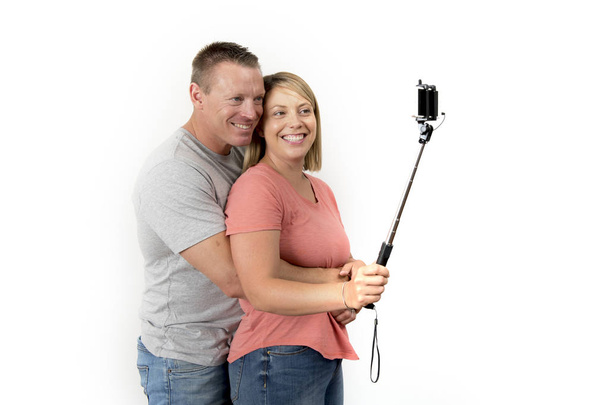 young beautiful happy and attractive romantic couple with husband and wife or girlfriend and boyfriend taking selfie self portrait photo with stick - Photo, image