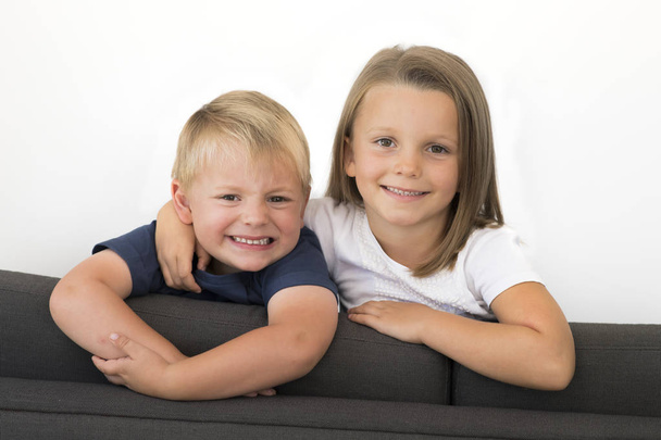7 years old beautiful little girl posing happy at home sofa couch with her small cute young 3 years old brother in siblings love relationship  - Zdjęcie, obraz