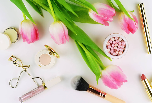 Makeup cosmetic accessories products pearl make up powder and brush, lipstick, pink tulips flowers on white background. Flat lay. Top view. Copy space  - Foto, Imagem