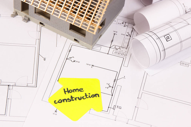 Pequeña casa en construcción y rollos de diagramas eléctricos o planos, concepto de casa de construcción
 - Foto, Imagen