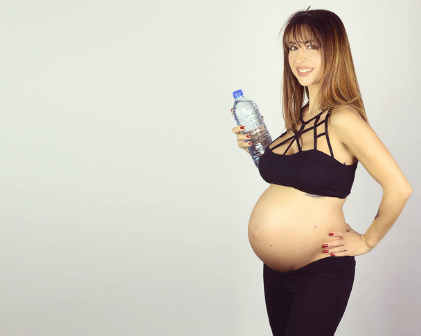 Jó látszó terhes nő gazdaság egy üveg víz a fehér háttér  - Fotó, kép