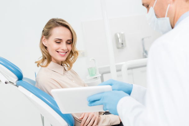 Médico y paciente sonriente mirando la pantalla de la tableta en la clínica dental moderna
 - Foto, Imagen