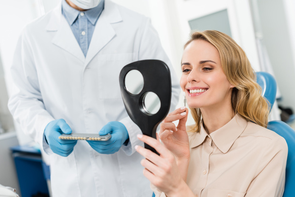Mulher escolhendo implante dental olhando para o espelho na clínica odontológica moderna
 - Foto, Imagem