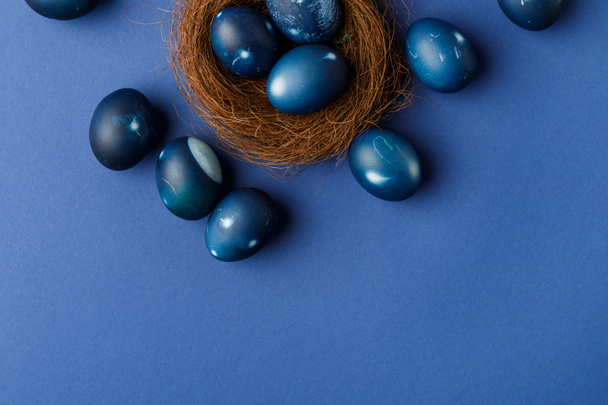 top view of blue painted easter eggs in decorative nest on blue surface - Photo, Image