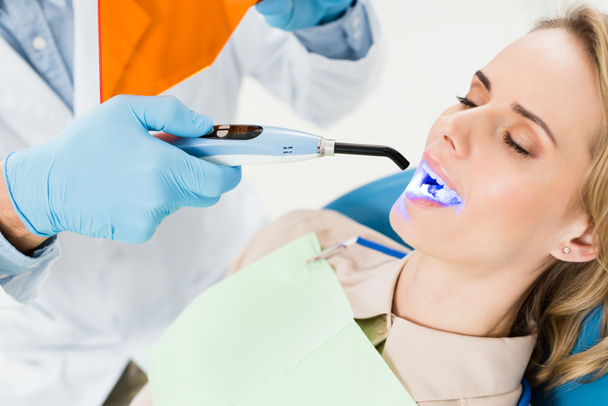 Dentist using uv lamp to treat patient teeth in modern dental clinic - 写真・画像