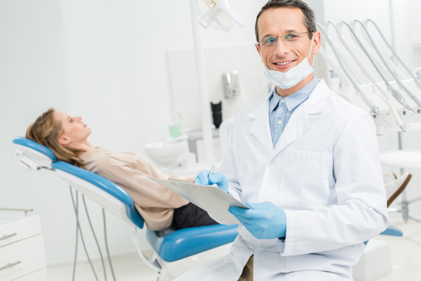 Arzt füllt Checkliste über weibliche Patientengesundheit in moderner Zahnklinik aus - Foto, Bild