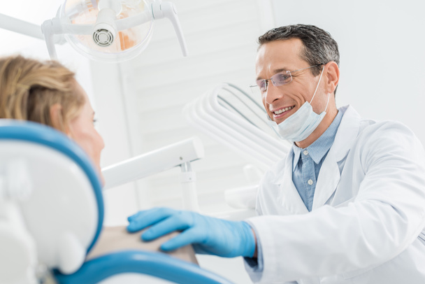 Médico sonriente consultando paciente femenina en clínica dental moderna
 - Foto, Imagen