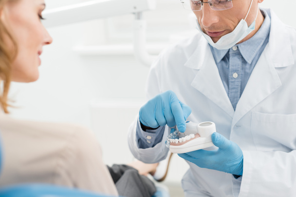 Médico mostrando modelo de mandíbulas a paciente femenina en clínica dental moderna - Foto, Imagen