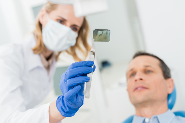 Mann berät sich mit Zahnarzt beim Röntgen in moderner Klinik - Foto, Bild