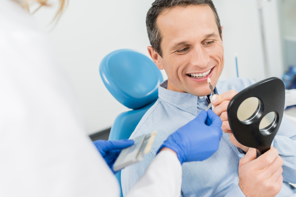 männlicher Patient, der sich für ein Zahnimplantat entscheidet, schaut in der modernen Zahnklinik in den Spiegel - Foto, Bild
