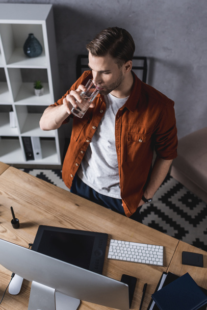 high angle view of young businessman looking at computer screen at office and drinking water - Fotoğraf, Görsel