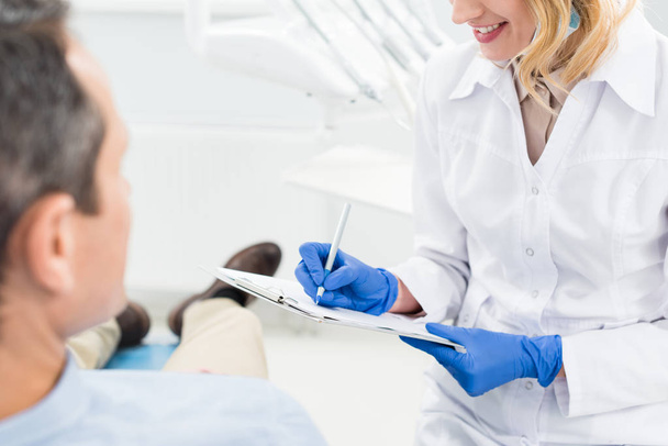 Medico femminile che registra la diagnosi mentre consulta il paziente in una moderna clinica dentale
 - Foto, immagini