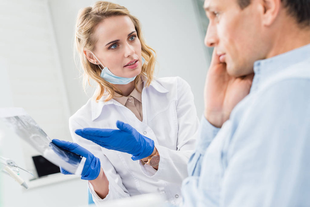 Hombre consultando con dentista mirando rayos X en clínica moderna
 - Foto, imagen