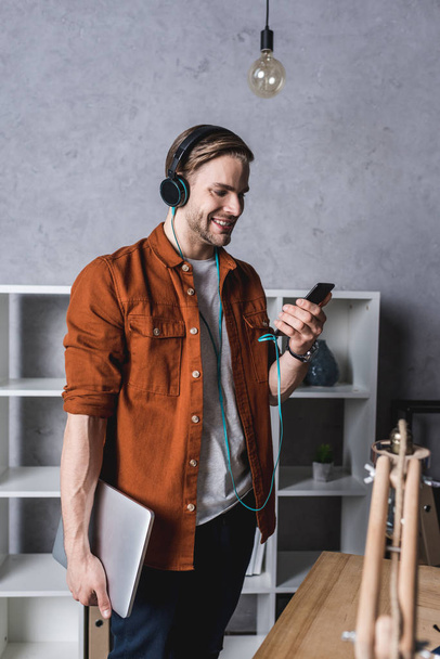 young man with laptop and smartphone listening music with headphones - Φωτογραφία, εικόνα