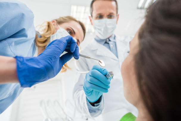 Médicos revisando dientes de paciente con espejo en clínica dental moderna
 - Foto, Imagen