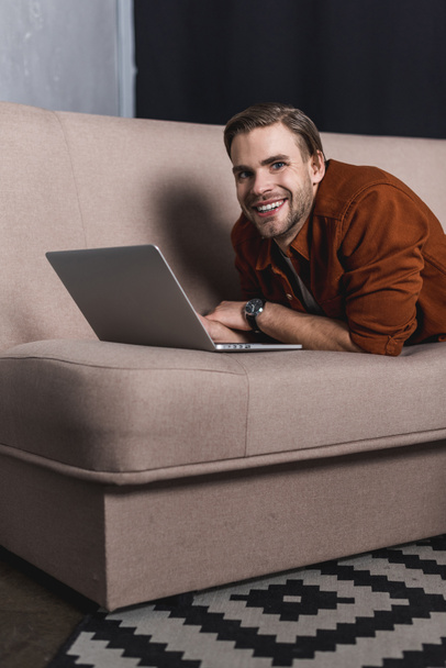 mladý šťastný muž pracovat s notebookem na gauči - Fotografie, Obrázek