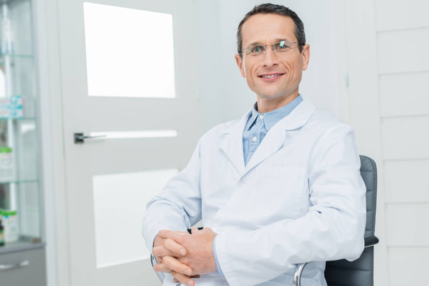Médico sonriente con las manos apretadas en la clínica moderna
 - Foto, Imagen