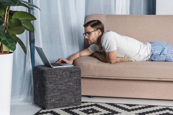 young attractive freelancer in pajamas working with laptop on couch - Photo, Image