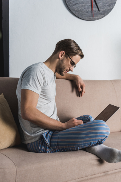 hymyilevä freelancer pyjamassa kannettavan tietokoneen avulla sohvalla
 - Valokuva, kuva