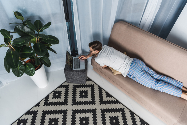 high angle view of freelancer in pajamas working with laptop on couch - Foto, afbeelding
