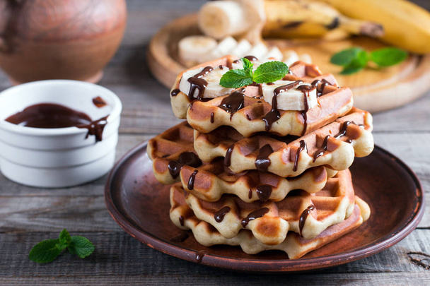 Belgialaiset vohvelit suklaasiirapilla ja banaaniviipaleella lautasella puupohjalla
 - Valokuva, kuva
