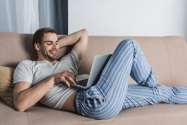 jeune freelance détendu en pyjama travaillant avec ordinateur portable sur le canapé
 - Photo, image