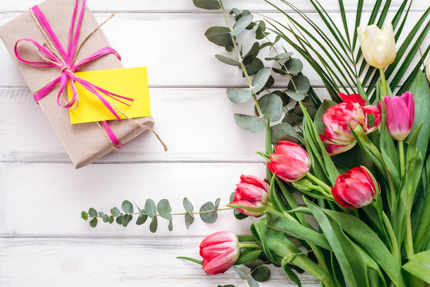 Composizione della confezione regalo con nota e bouquet di tulipani su sfondo di assi di legno
 - Foto, immagini