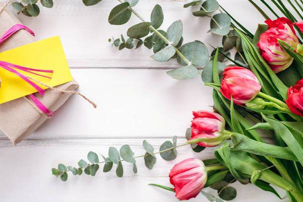Decorative composition of gift box with note and tulip bouquet on wooden planks background - Photo, Image