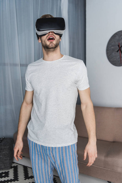 megdöbbent fiatalember pizsamában és a virtuális-valóság sisak - Fotó, kép