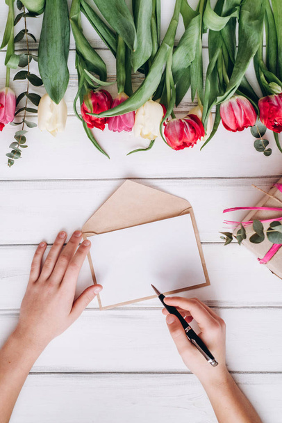 Ansicht der Frau Schreiben auf weißem Papier und bunte Tulpen auf dem Hintergrund - Foto, Bild