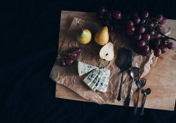 view of Blue cheese Roquefort with fresh pears, grapes and Vintage silver spoons on Parchment paper on black background - Fotografie, Obrázek