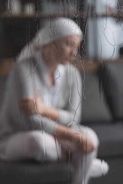close-up view of glass with raindrops and sick mature woman behind  - Foto, immagini