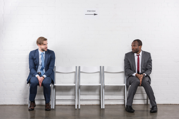 scared multiethnic businessmen looking at each other while waiting for job interview - 写真・画像