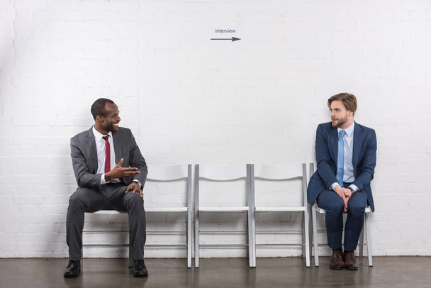 smiling african american businessman looking at scared colleague while waiting for job interview - Foto, Bild