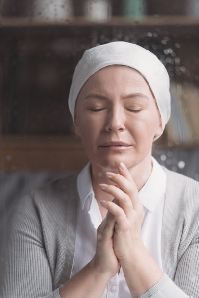 portrait of sick mature woman in kerchief praying with closed eyes - Fotó, kép