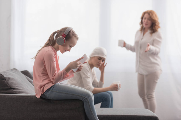 criança em fones de ouvido usando tablet digital enquanto a mãe doente e avó falando atrás
   - Foto, Imagem